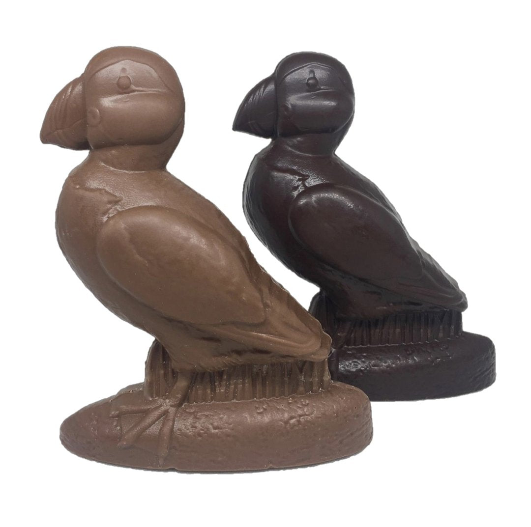 Two chocolate figures shaped like puffin birds, one made of milk chocolate and the other made of dark chocolate, both standing on oval bases.