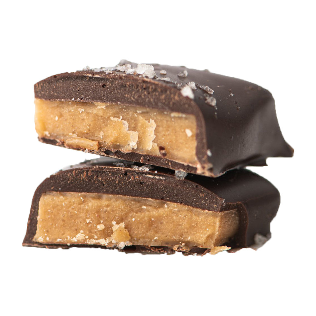 Two pieces of chocolate candy filled with a creamy peanut butter center, stacked on each other, with a sprinkle of coarse salt on top, isolated on a white background.