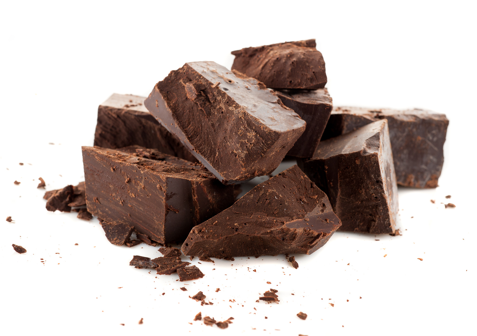 Chunks of dark chocolate stacked together on a white background, with small pieces and crumbs scattered around them.