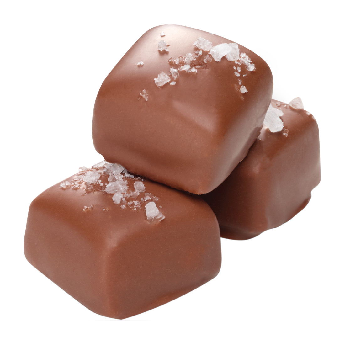 Three milk chocolate caramels stacked together, each topped with a sprinkling of coarse sea salt, on a white background.