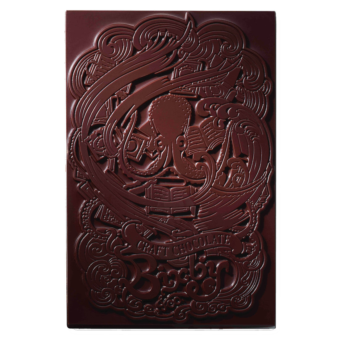 A dark chocolate bar features an embossed design of an octopus reading a book, with swirling patterns and the words Craft Chocolate and Brooklyn visible on the surface.