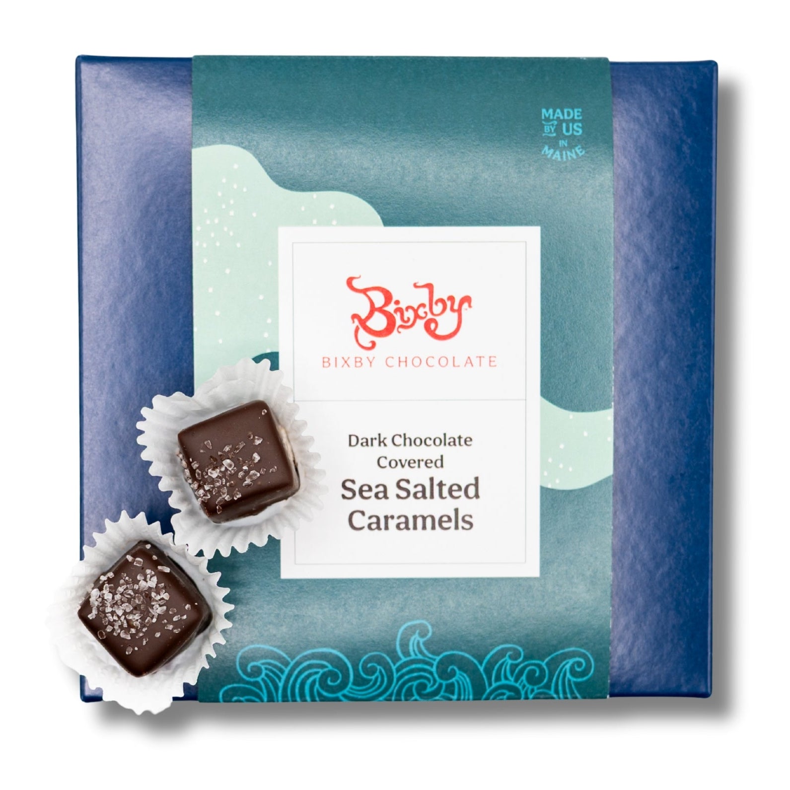 A blue box of Bixby Chocolate Dark Chocolate Covered Sea Salted Caramels with an illustrated wave design. Two caramel pieces in paper cups are placed in front, topped with sea salt crystals.