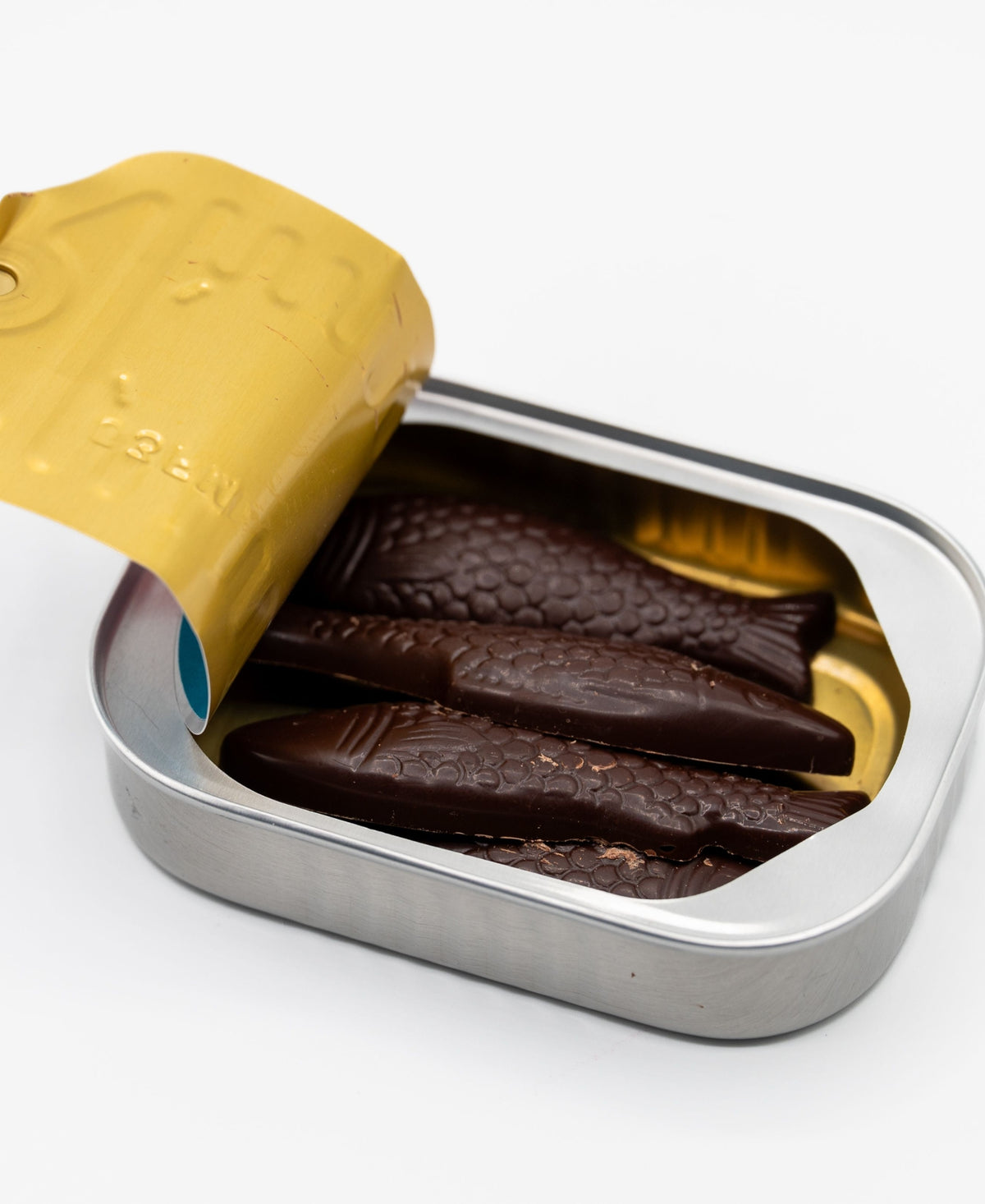 An open tin of Bixby Chocolates’ Chocolate Sardines, with a gold lid, displays fish-shaped artisanal chocolates neatly arranged inside—an ideal Maine souvenir—set against a white background.