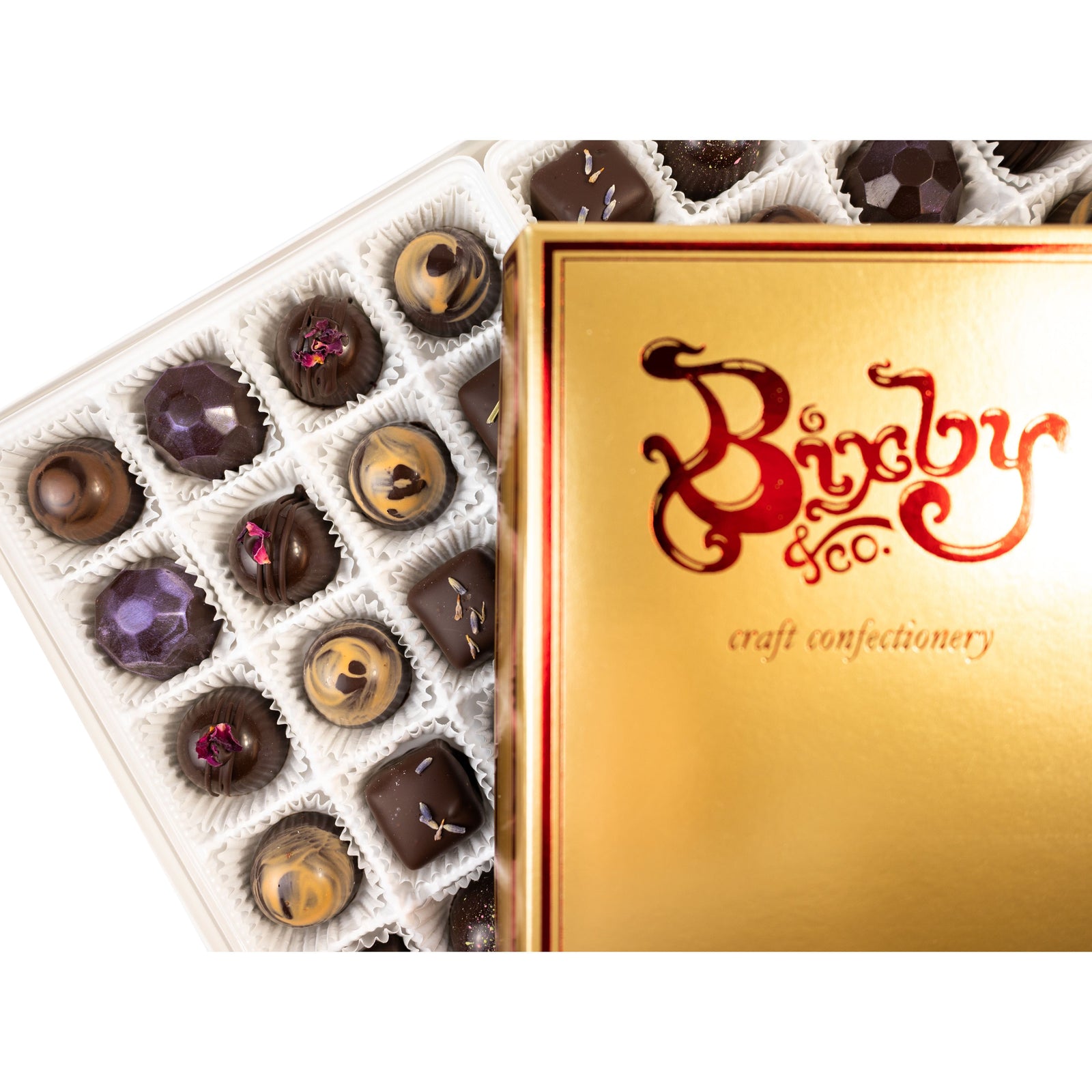 An open box of assorted chocolates with a gold lid labeled Bixby & Co. craft confectionery, showing various dark and milk chocolates arranged in a grid.