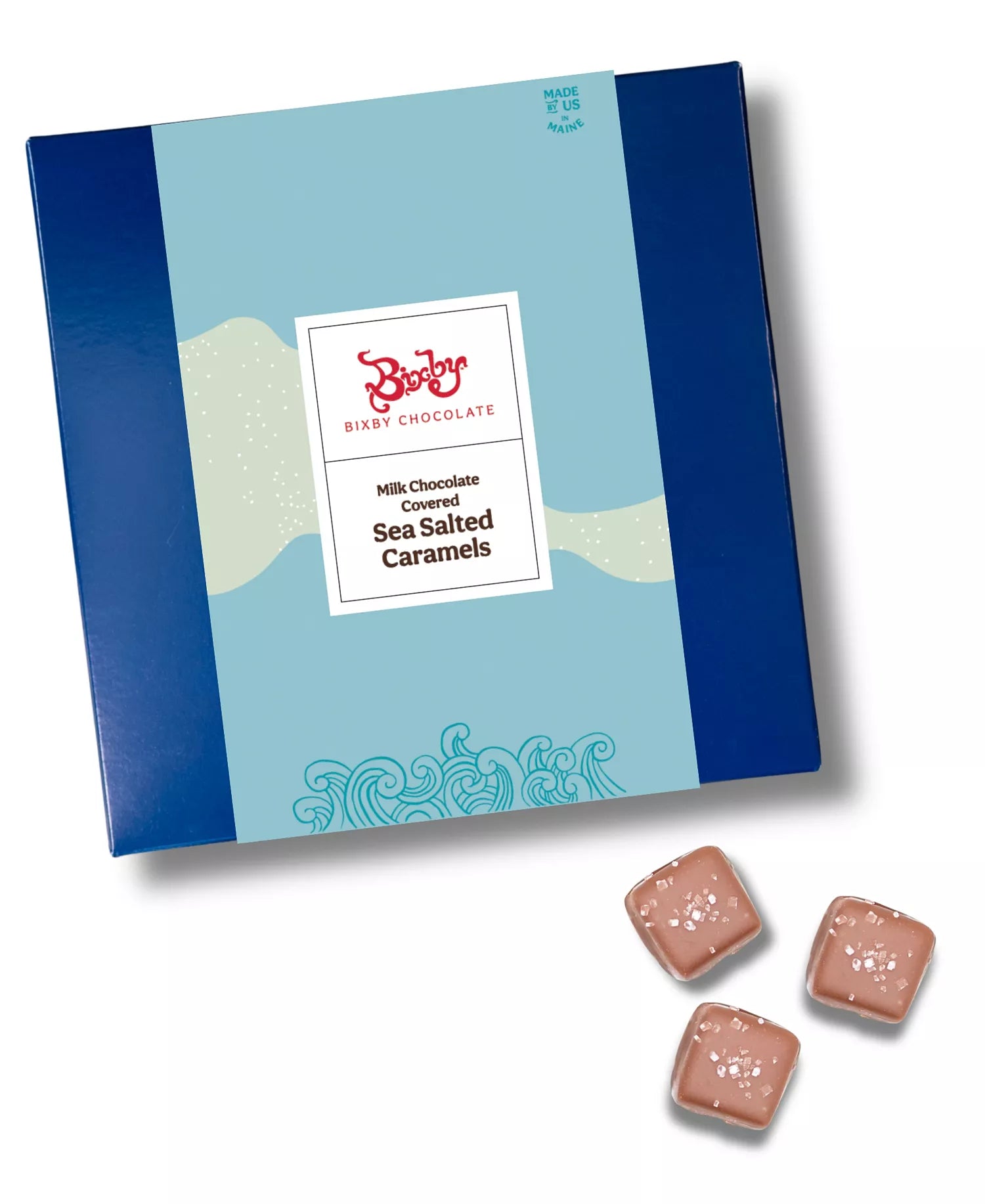 A blue box of Bixby Chocolate Milk Chocolate Covered Sea Salted Caramels sits next to three caramel pieces topped with sea salt on a white background.