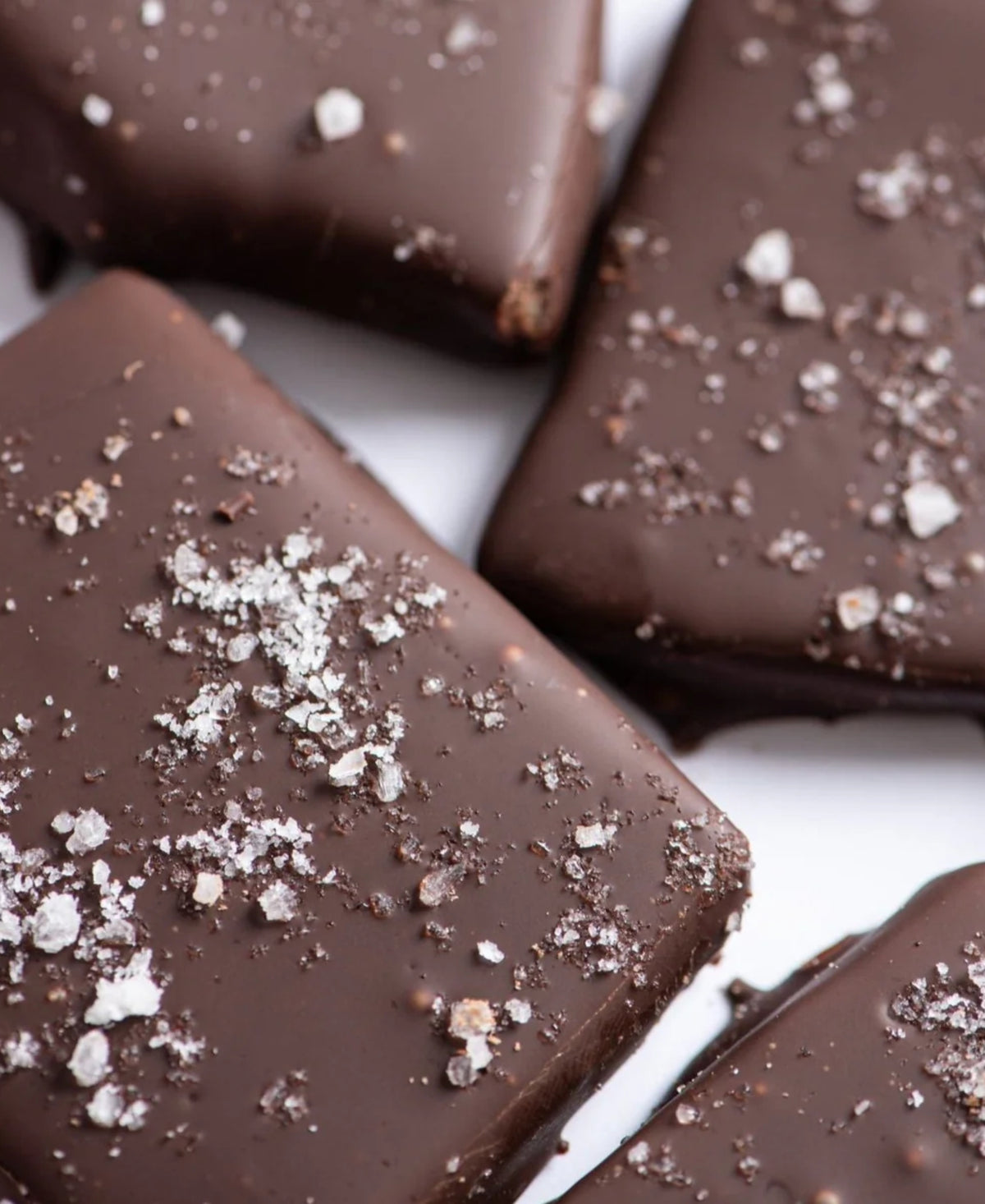 Close-up of Bixby Chocolates' Dark Chocolate Toffee squares, sprinkled with coarse sea salt and arranged together on a white surface.