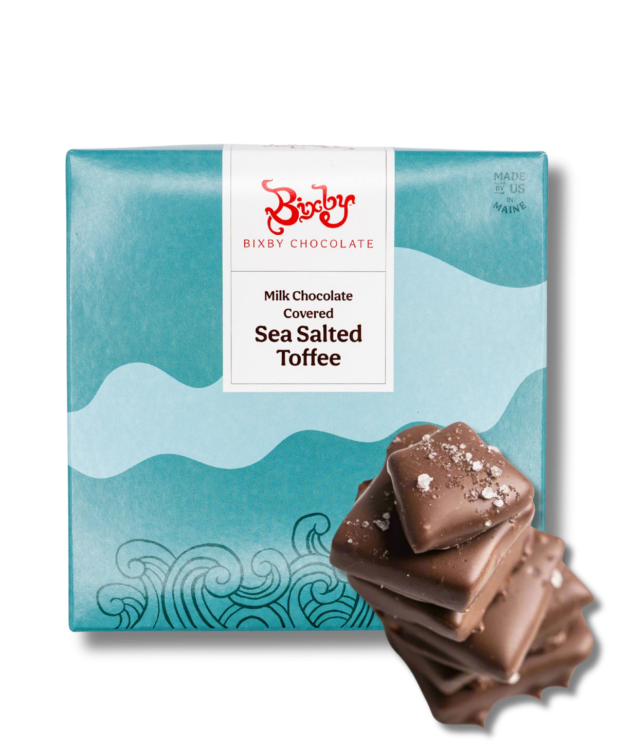 A blue and white box labeled “Bixby Chocolates Milk Chocolate Toffee” with a wave design sits behind a small stack of sea salt toffee pieces.