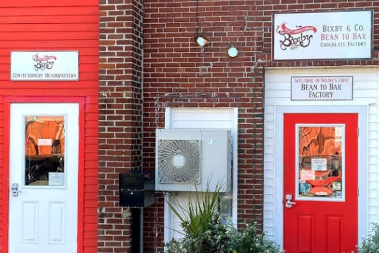 Exterior of a brick building with two red-trimmed doors. Signs read Confectionery Headquarters and Bixby & Co. Bean to Bar Chocolate Factory. An air conditioning unit is mounted between the doors.