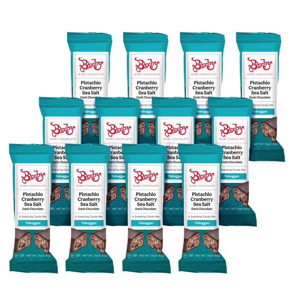 Twelve teal-wrapped Bixby Chocolates Toboggan® bars—Dark Chocolate, Pistachios, Cranberries, and Maine Sea Salt (Vegan)—are arranged in rows on a white background.