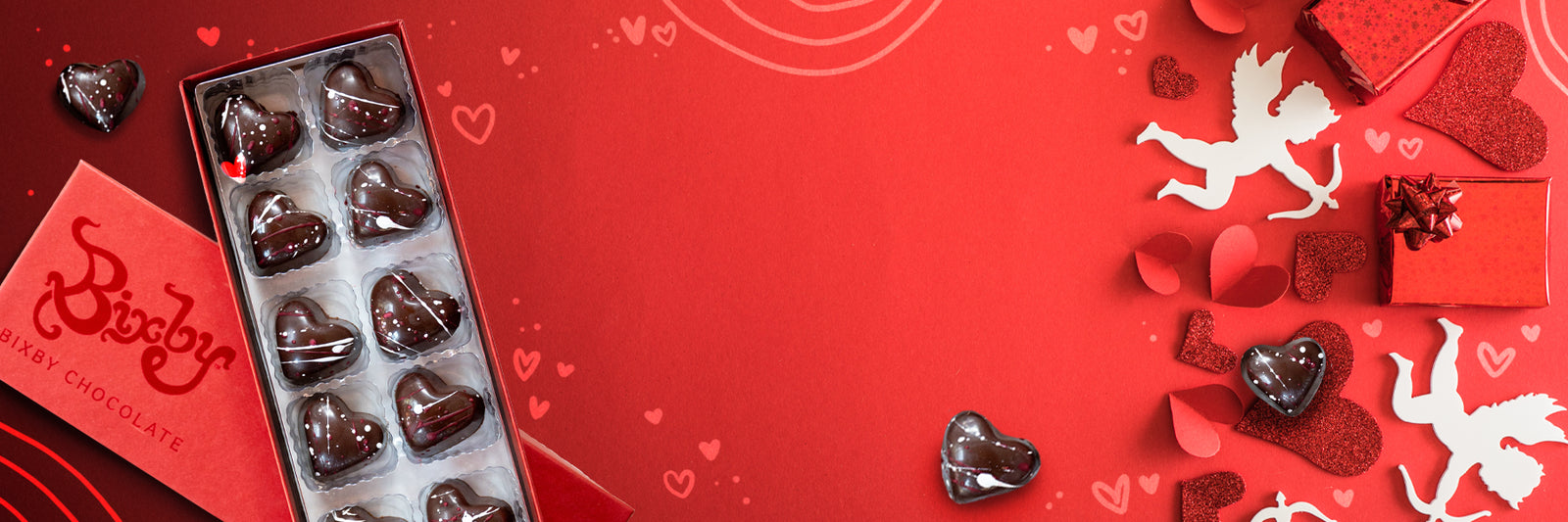 A red box of heart-shaped chocolates sits on a red surface with white and glittery heart decorations, a gift box, and white cupid silhouettes, creating a festive Valentines Day theme.