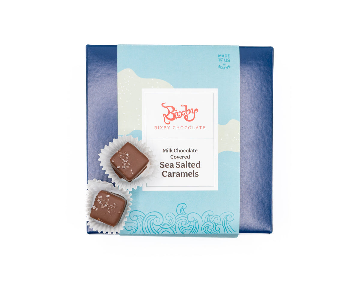 The Chocolate Sea Salted Caramels Gift Box by Bixby Chocolates features milk chocolate covered sea salted caramels, topped with two unwrapped artisanal chocolates, all displayed against a white background.