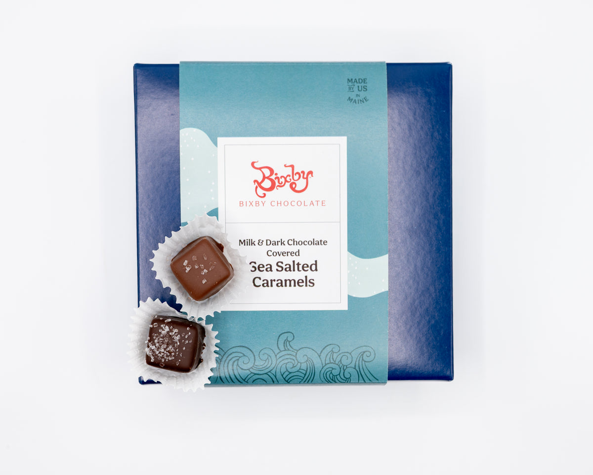 The Chocolate Sea Salted Caramels Gift Box by Bixby Chocolates features milk and dark chocolate covered sea salted caramels, with two unwrapped pieces in paper cups displayed in front of the box.