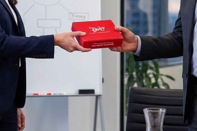 Businesswoman passing a red box of Bixby chocolate to a businessman in a corporate office.