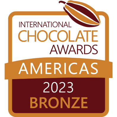 A badge displaying International Chocolate Awards Americas 2023 Bronze with a stylized cocoa pod at the top. The background uses shades of brown, bronze, and gold.