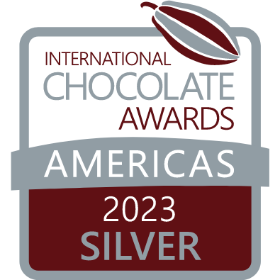 International Chocolate Awards Americas 2023 Silver medal logo, featuring a stylized cocoa pod at the top and text in maroon and gray on a shield-like background.