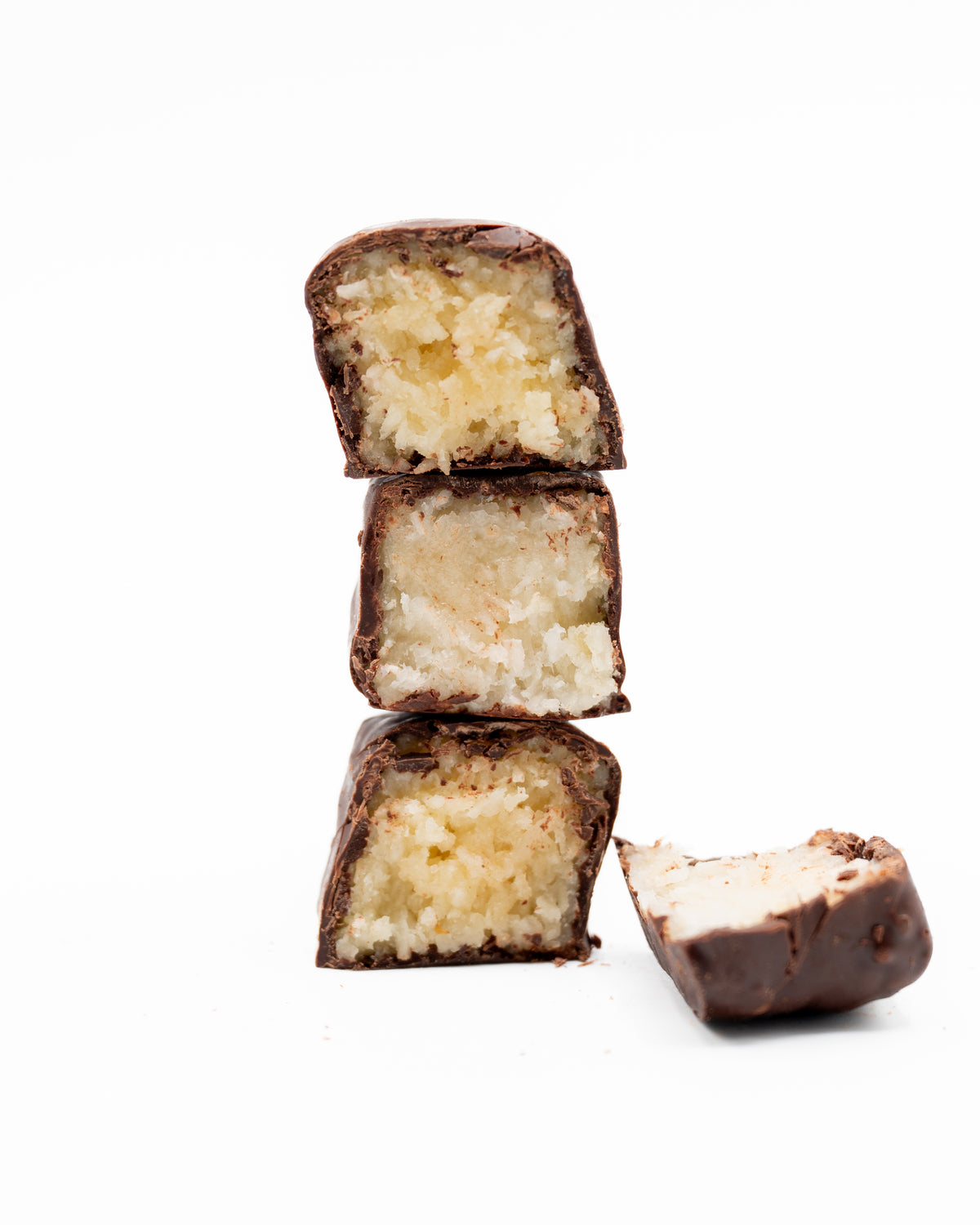 Three stacked Bixby Chocolates Needhams, with a fourth partially eaten beside them, rest on a white background. The coconut filling is visible in each bar—a classic Maine treat.