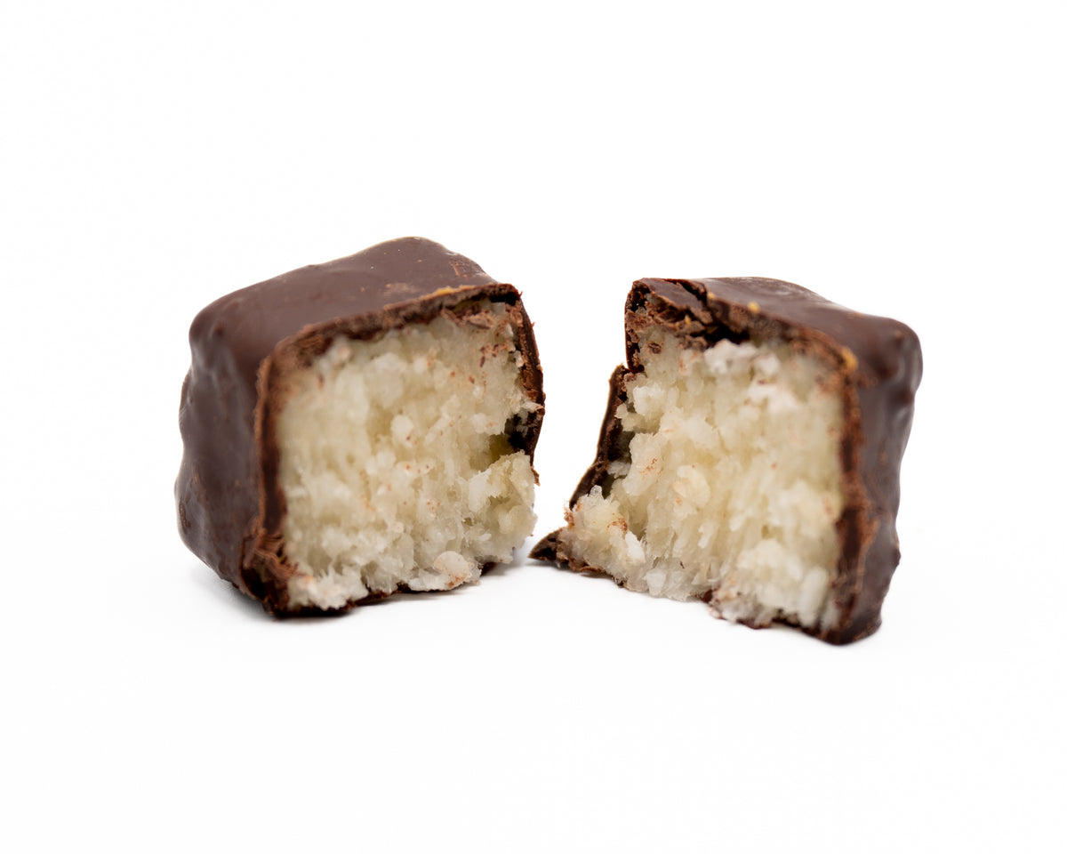 A Bixby Chocolates Needhams bar, split in half to reveal its white coconut filling, is displayed against a plain white background.