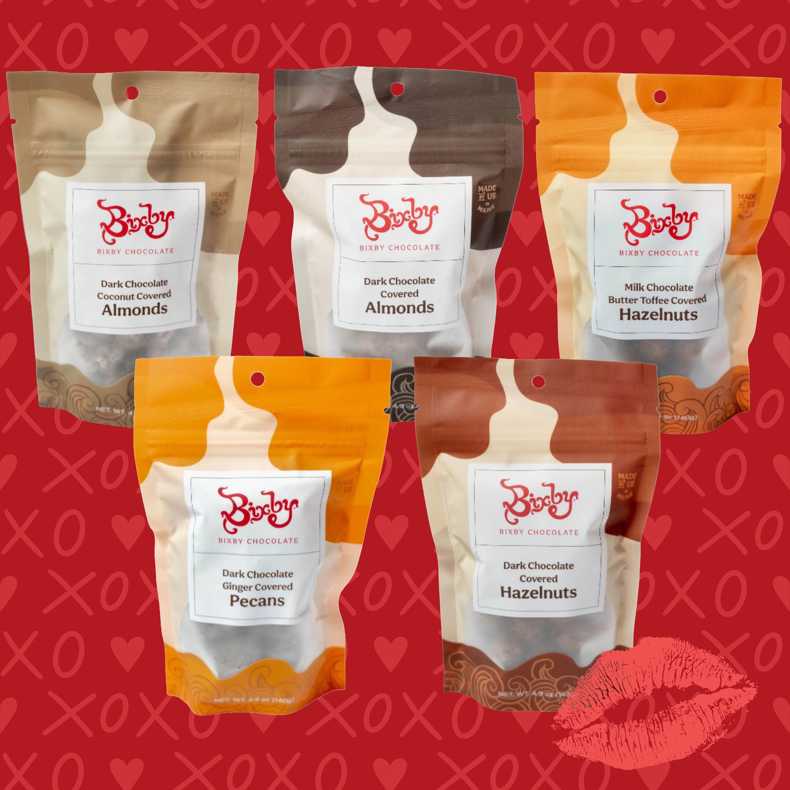 Five Bixby chocolate nut snack pouches are displayed on a red background with hearts and a kiss mark. Flavors include dark chocolate coconut almonds, dark chocolate almonds, milk chocolate hazelnuts, ginger pecans, and butter toffee hazelnuts.