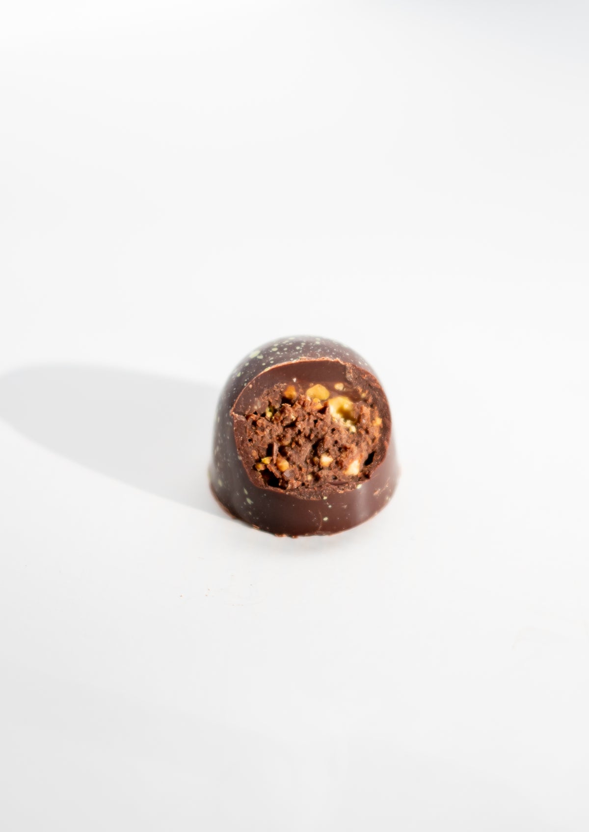 A Pistachio Dark Chocolate Bon Bon (Vegan) by Bixby Chocolates, with a bite revealing its nutty center, sits on a white background—a true plant-based treat from the Gift Box collection.