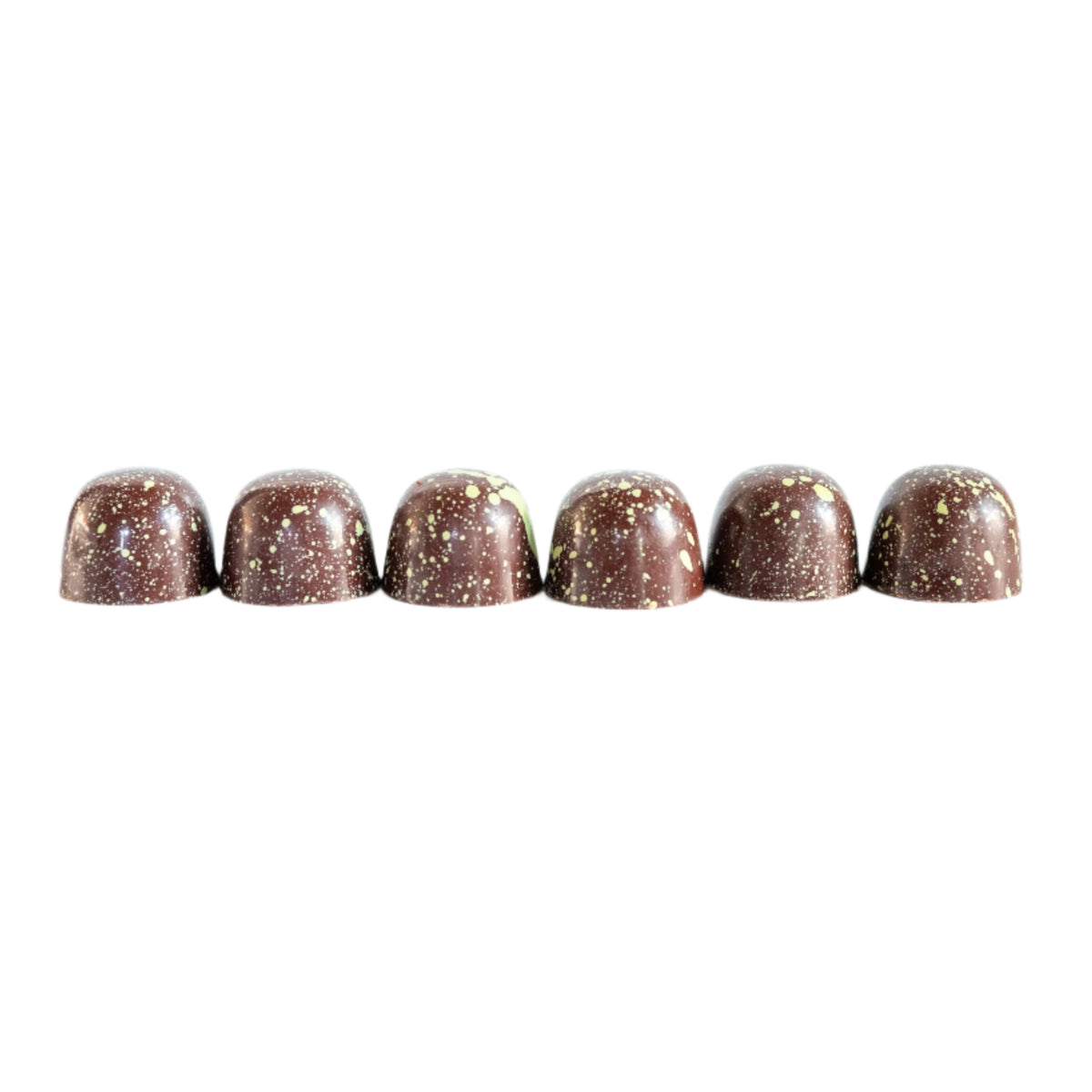 Six round, glossy Pistachio Dark Chocolate Bon Bons by Bixby Chocolates, adorned with gold speckles, are lined up on a white background—a luxurious vegan gift box treat for plant-based chocolate lovers.