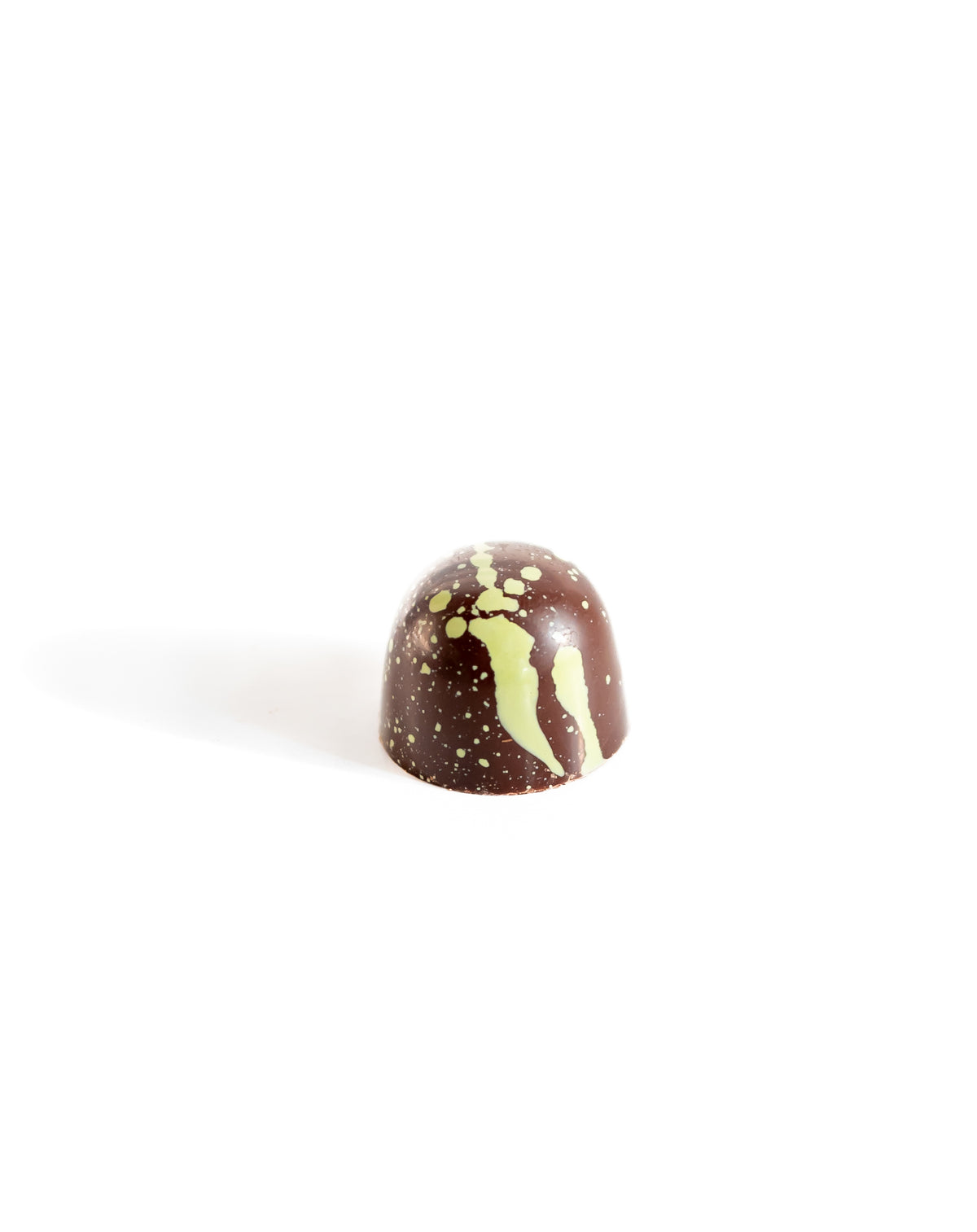 A vegan dome-shaped Pistachio Dark Chocolate Bon Bon from Bixby Chocolates, adorned with yellow-green splatters, sits on a white background—plant-based and inspired by Pistachio Gianduja.