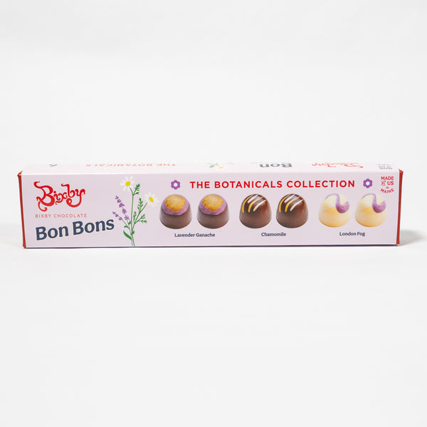 A long rectangular box of Biscuit Bon Bons chocolates from The Botanics Collection, displayed on a clean white background. The box is light pink with illustrations of lavender flowers and images of four decorated chocolate bonbons: Lavender Gochache, Chanomille, London Fog, and White Chantilly.