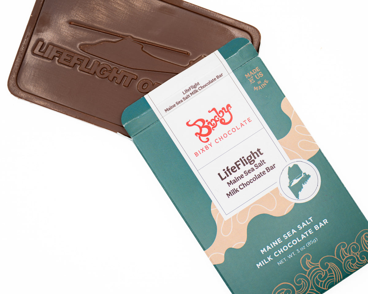 A Bixby Chocolates LifeFlight Maine Sea Salt Milk Chocolate Bar is partially unwrapped, revealing a bar embossed with a helicopter and “LIFEFLIGHT OF MAINE”—a tribute to emergency air transport heroes.
