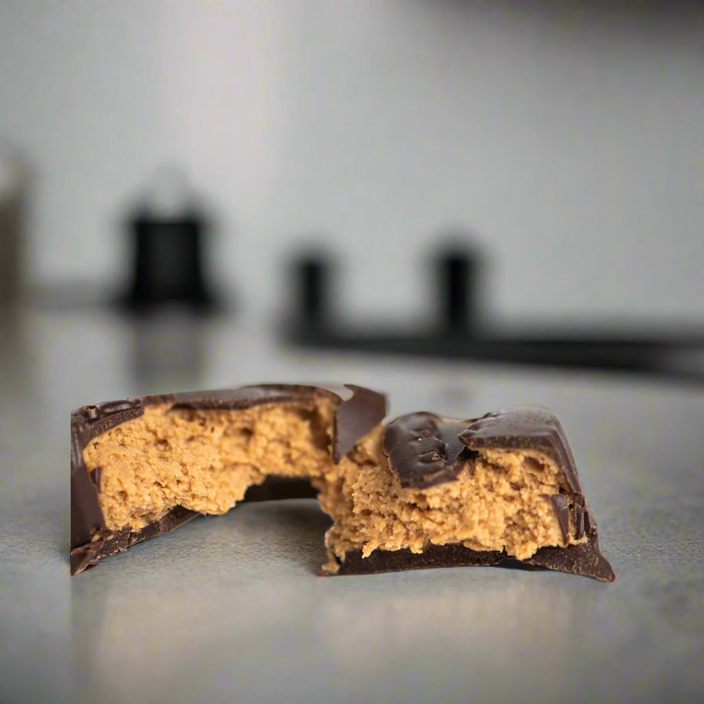 A close-up of Bixby Chocolates' Peanut Butter Lobster Claws, split in half to reveal the creamy peanut butter ganache filling inside, sits on a smooth, light surface with a softly blurred background.