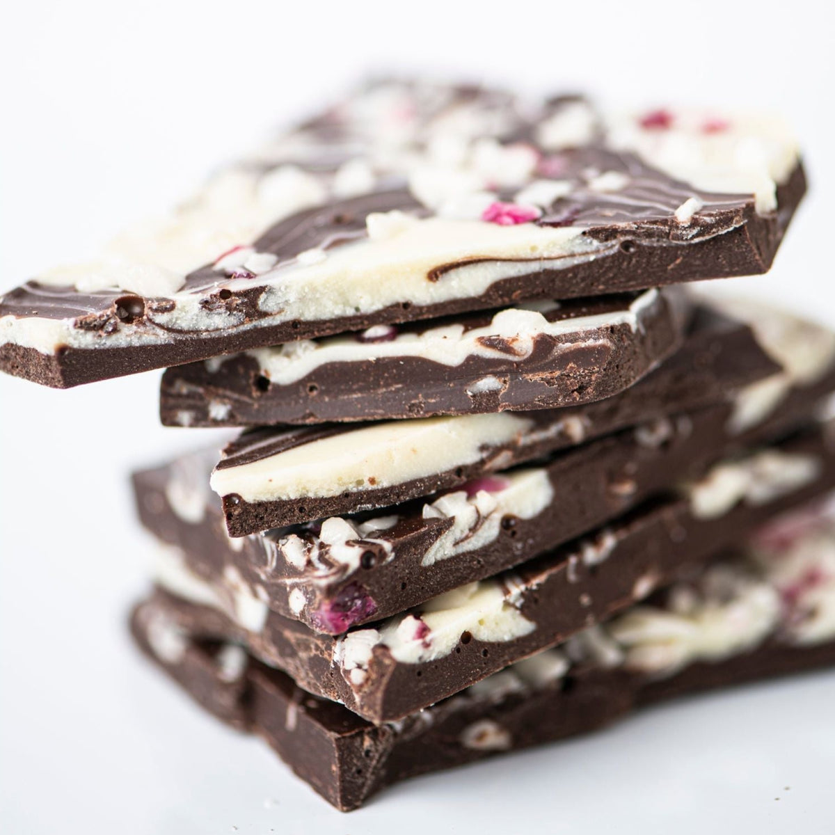 Bixby Chocolates Peppermint Bark features artisan chocolate pieces with white chocolate swirls and red candy bits, evoking classic holiday flavors—an ideal festive gift, beautifully arranged against a white background.