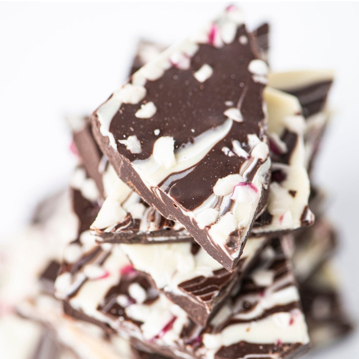 A close-up of Bixby Chocolates Peppermint Bark, featuring swirled white chocolate and peppermint candy bits—an ideal artisan holiday gift—set against a white background.