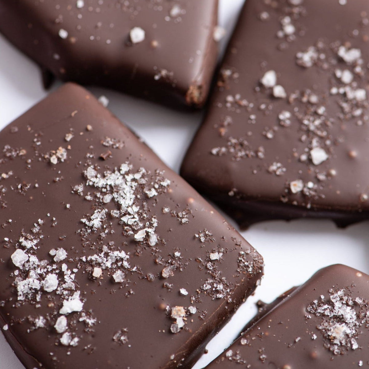 Close-up of Bixby Chocolates Dark Chocolate Toffee pieces topped with coarse Maine sea salt, arranged on a white surface.