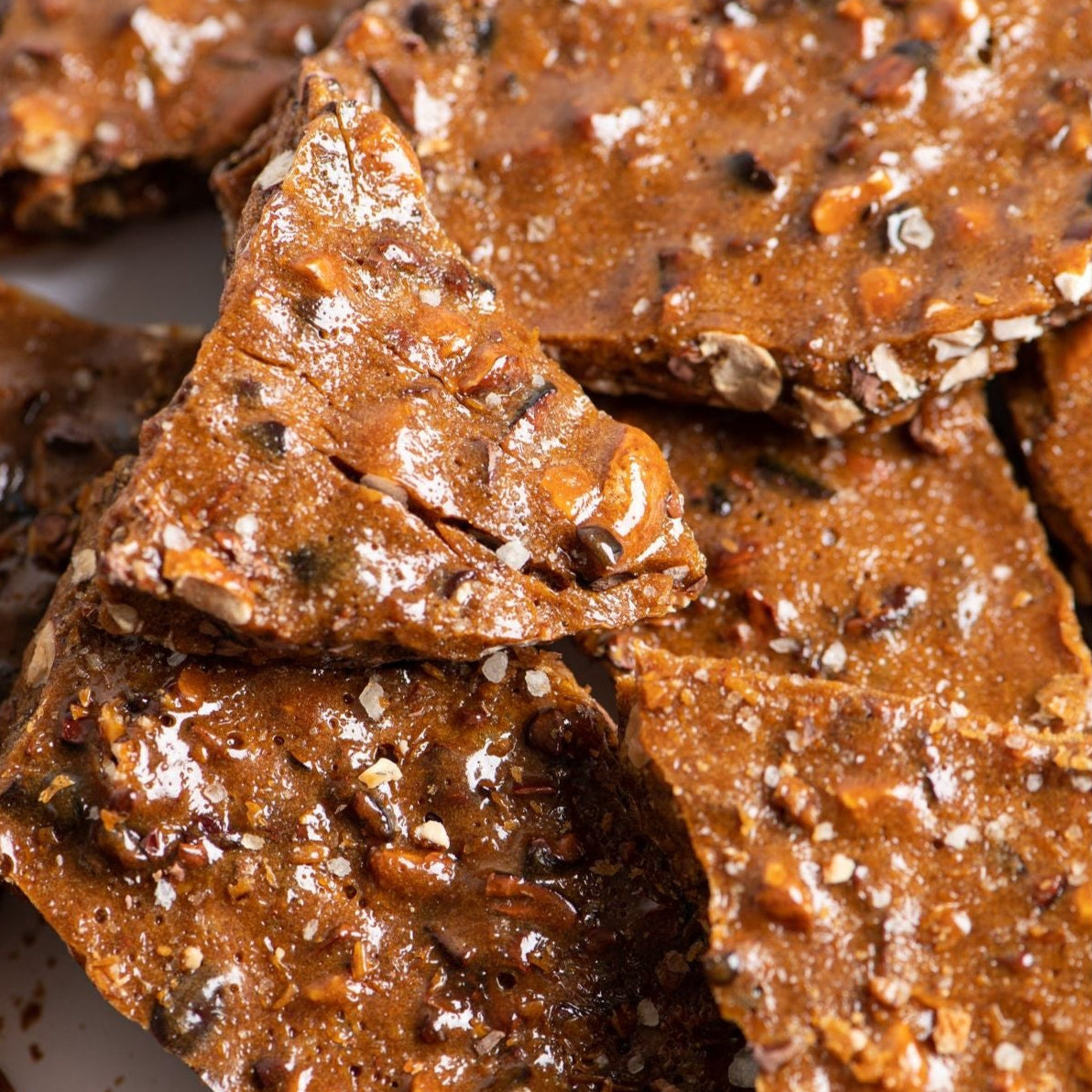 Close-up of several pieces of Bixby Chocolates' Allagash Beer Brittle, featuring a shiny, textured surface with visible chunks of nuts embedded in the caramelized candy.