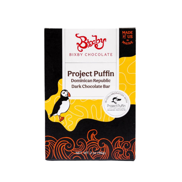 The Bixby Chocolates Organic Project Puffin 70% Dark Chocolate Bar features a puffin illustration, bold yellow-orange waves, and spotlights its organic Dominican Republic cacao. Made in Maine, it supports seabird conservation.