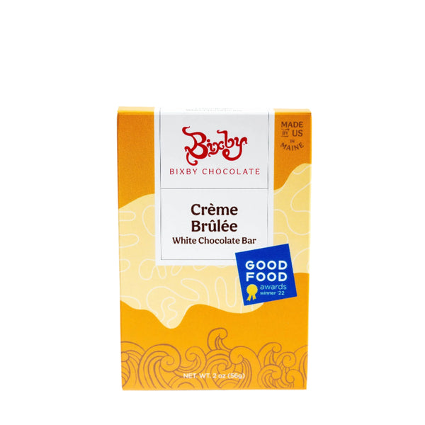A box of Bixby Chocolates Organic Crème Brûlée White Chocolate Bar with yellow-orange abstract designs, a "GOOD FOOD awards winner '22" label, and “Made in Maine, USA”—crafted with organic ingredients and real vanilla bean.