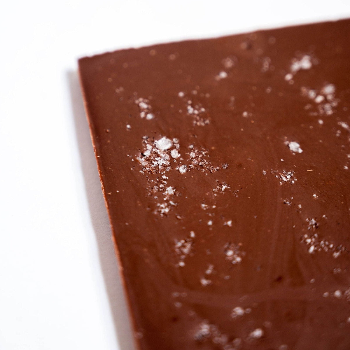A close-up of Bixby Chocolates’ Organic Milk Chocolate Maine Sea Salt Bar, sprinkled with coarse sea salt, set against a white background.