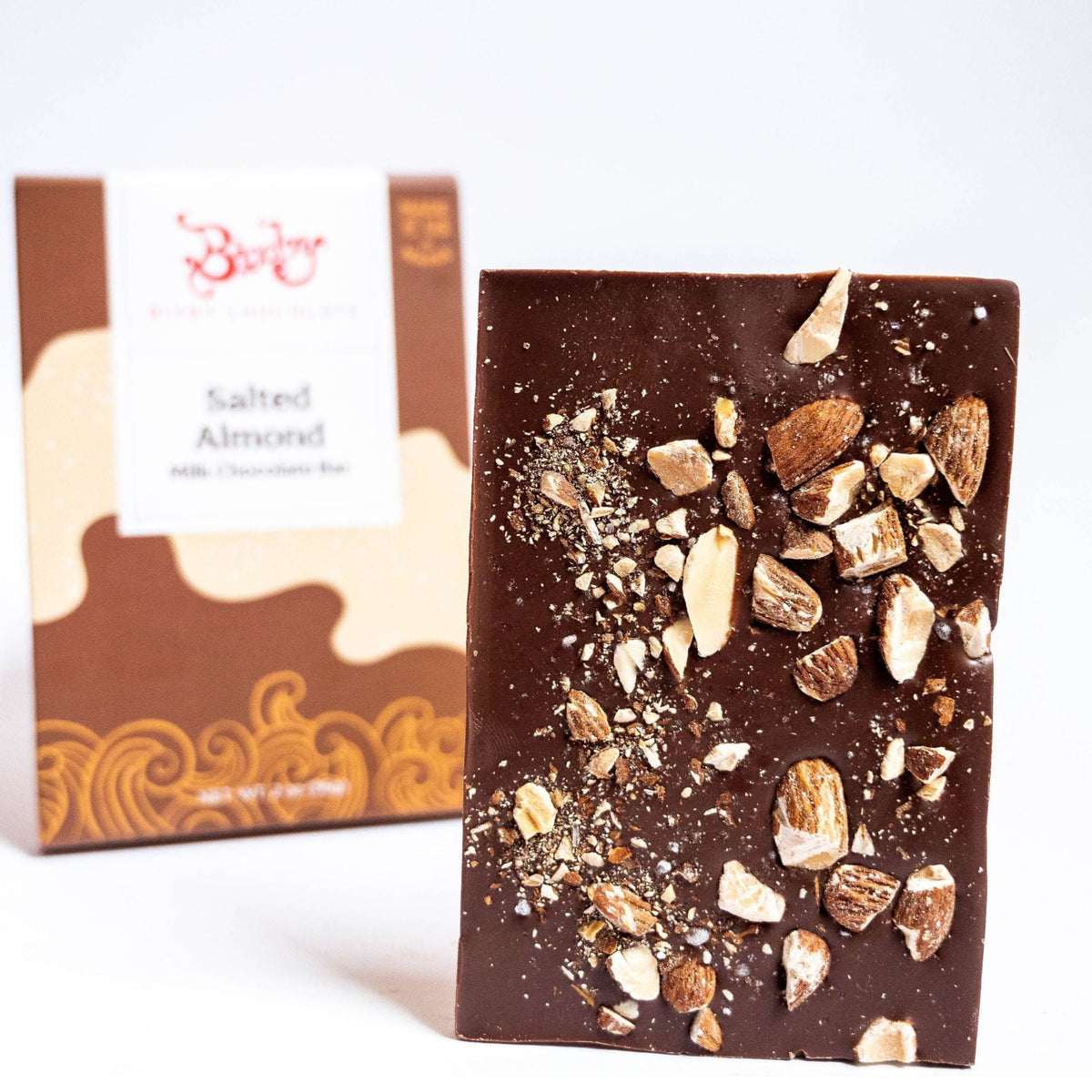 The Bixby Chocolates Milk Chocolate Salted Almond Chocolate Bar stands upright, its wavy brown and cream packaging blurred in the background.