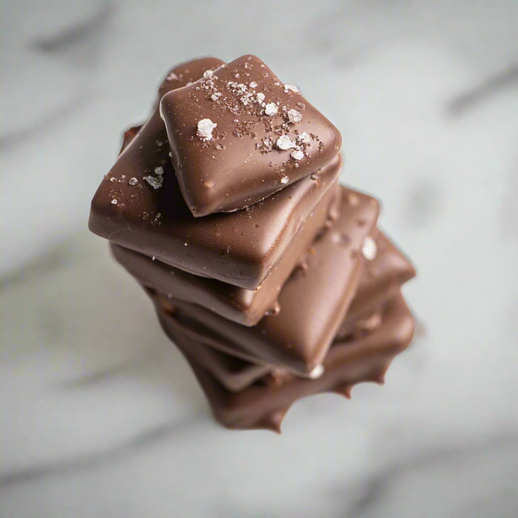 A stack of Bixby Chocolates Milk Chocolate Toffee sprinkled with flaky sea salt, photographed from above on a light marble surface.
