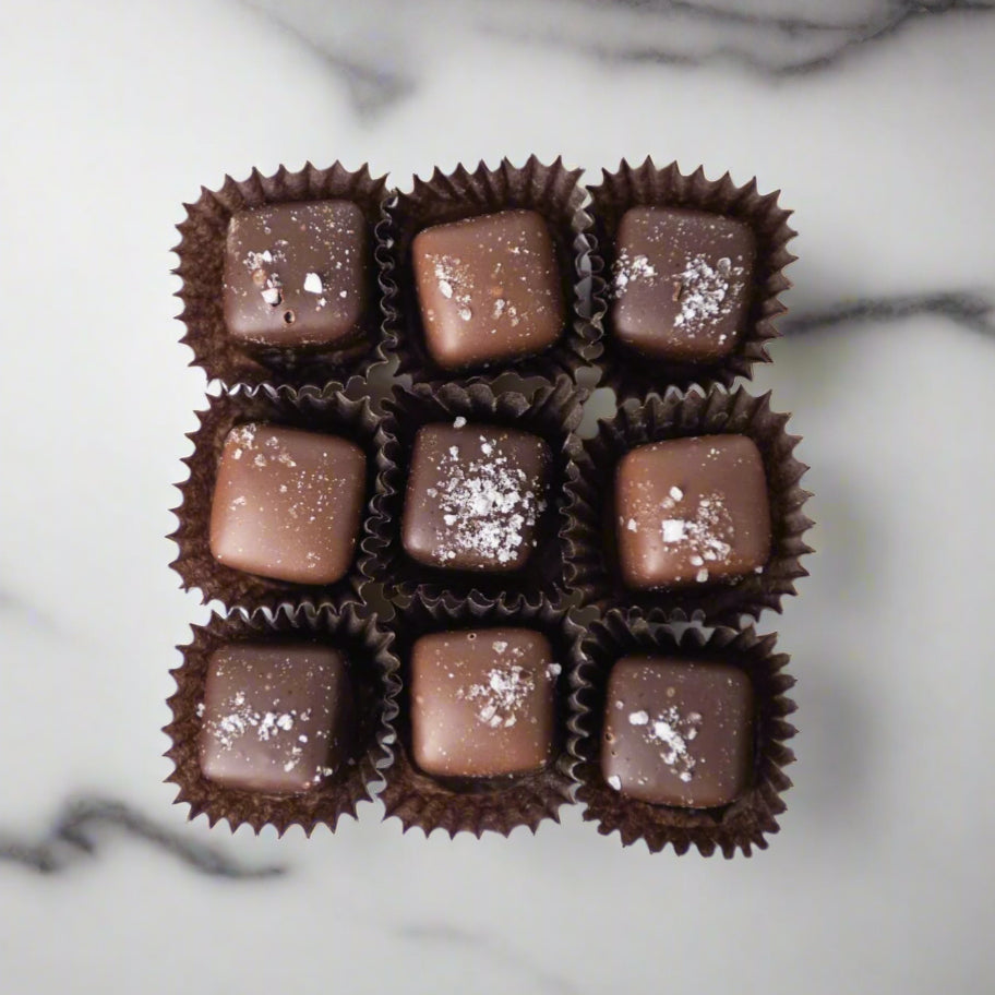 The Bixby Chocolates 32 piece Milk & Dark Chocolate Sea Salted Caramel Gift Box features gluten-free caramel truffles in brown paper cups, each topped with a sprinkle of sea salt for a perfect sweet and salty treat.