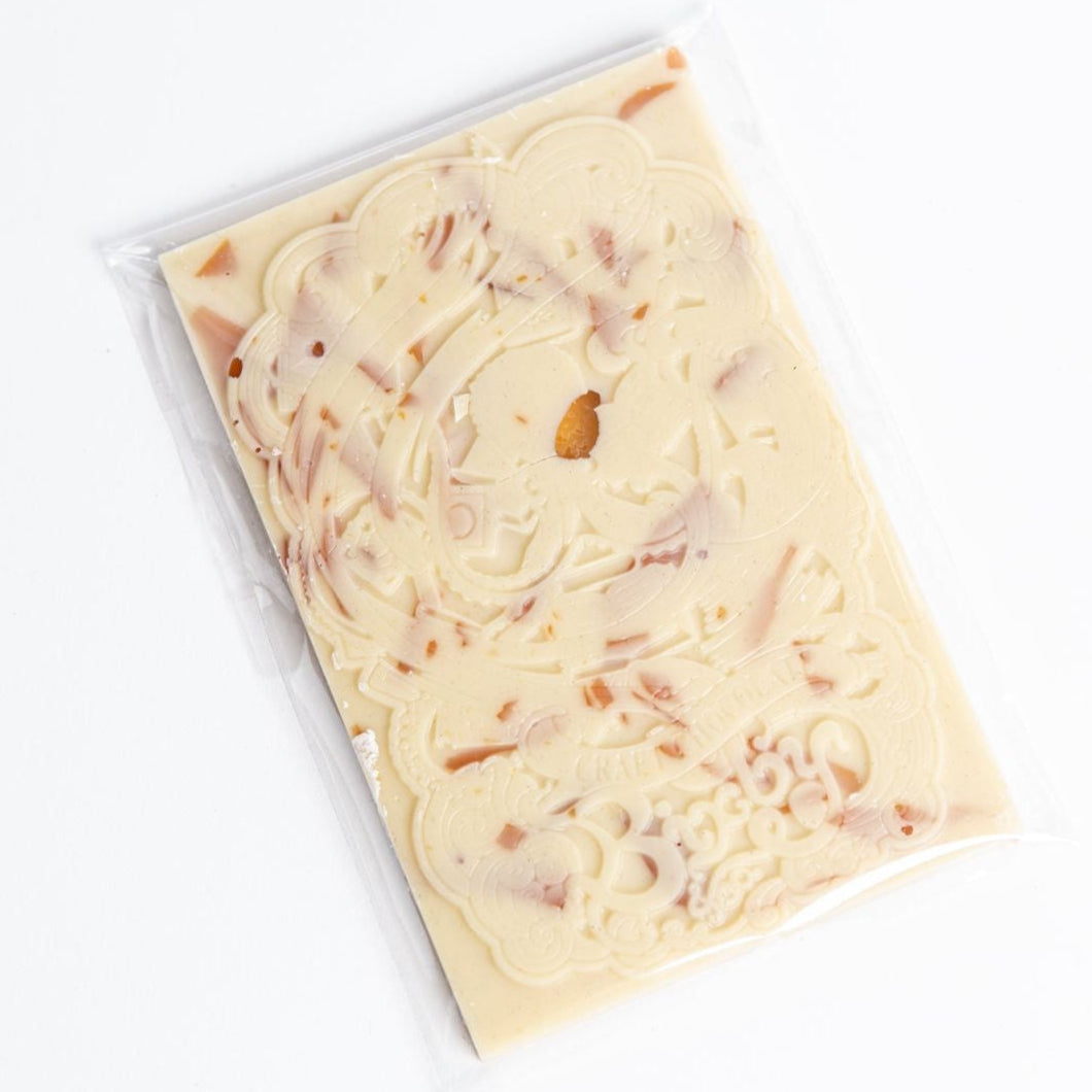 The Organic Crème Brûlée White Chocolate Bar by Bixby Chocolates features vanilla bean and organic ingredients, decorative swirls, visible caramel pieces, and comes in clear plastic packaging displayed on a white background.
