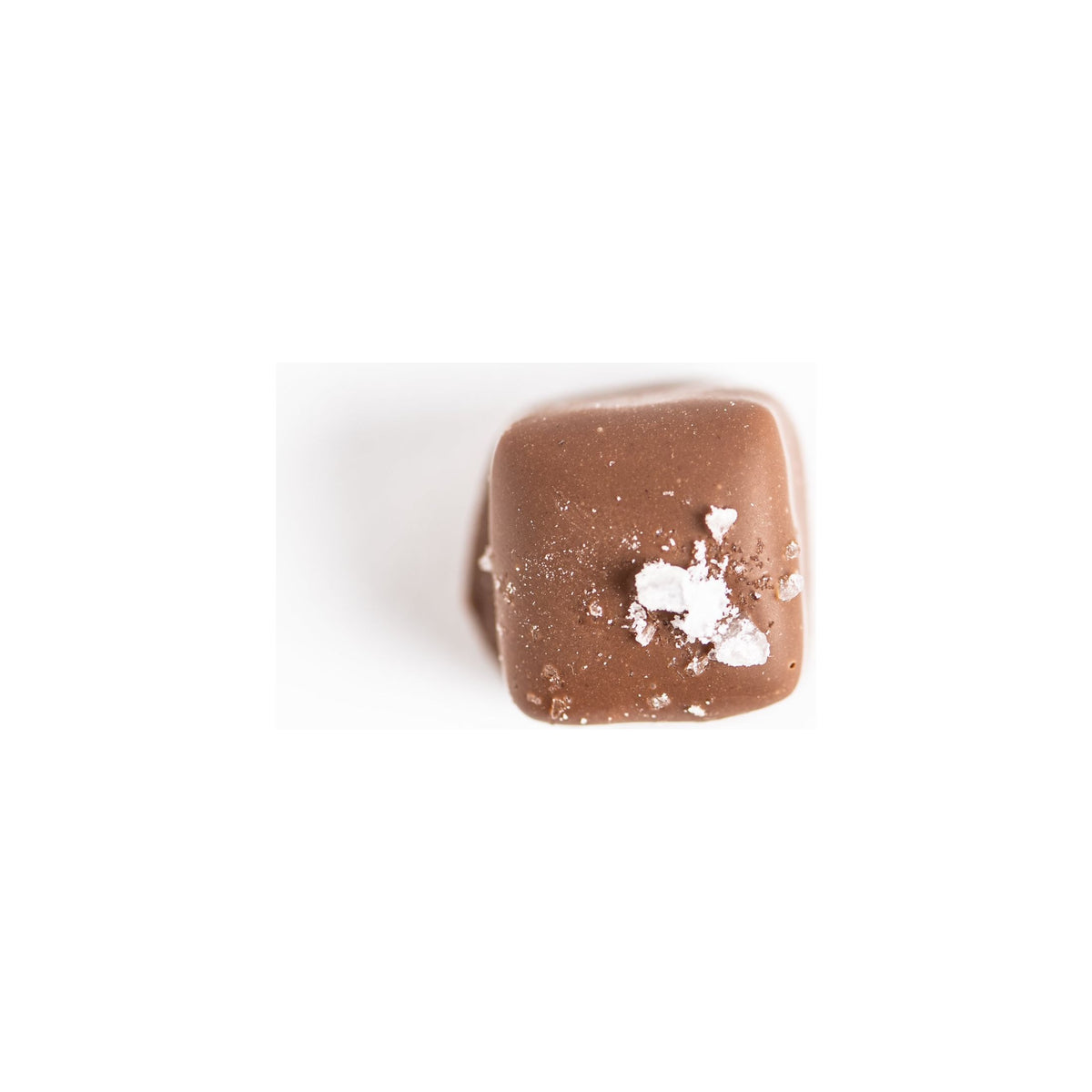 A piece of Bixby Chocolates' Milk Chocolate Sea Salt Caramels--6 Pouches is shown on a white background, topped with sea salt flakes.